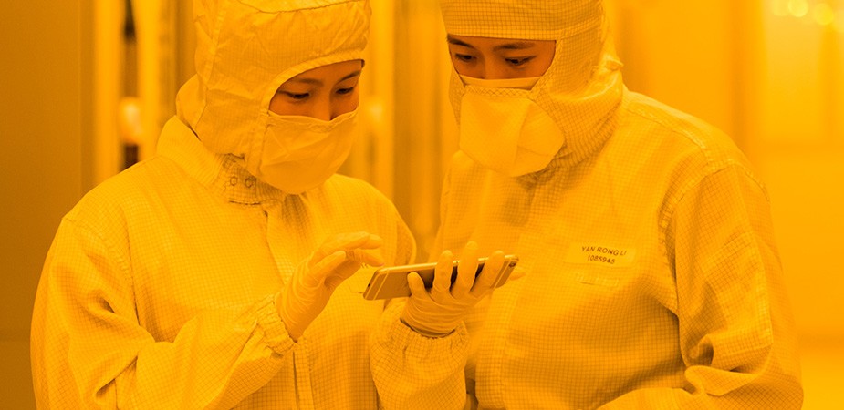 Two Fab co-workers looking at a phone, dressed in their clean room suits