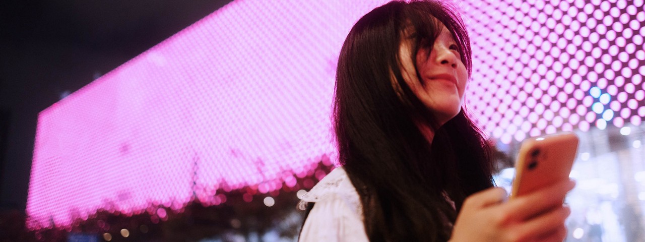 Woman using her phone at night, standing in front of a wall of LED lights